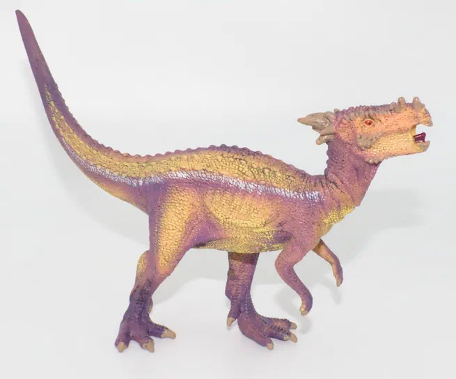 Un jouet de dinosaure à quatre pattes, aux couleurs violettes et jaunes sur fond blanc.
