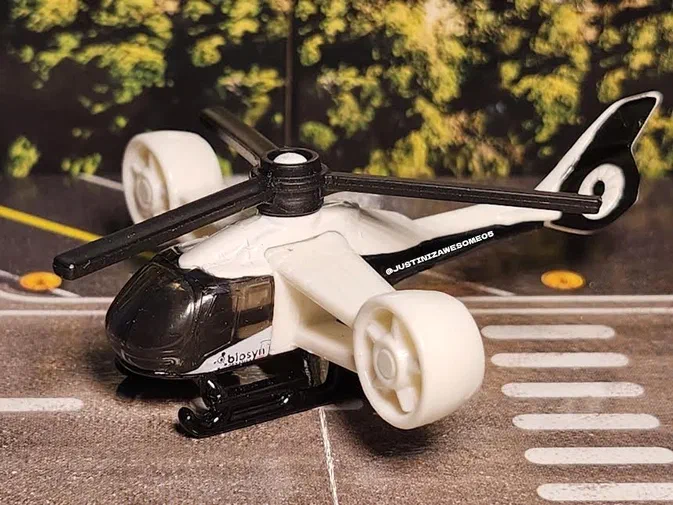Hélicoptère blanc Matchbox Rapid Rescue Copter posé sur une route avec des arbres en arrière-plan.