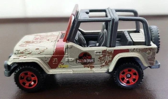 Petite voiture de collection Matchbox Jeep Wrangler beige avec des taches de boue et un logo Jurassic Park sur la portière.