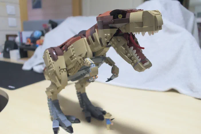 Un modèle de dinosaure T-Rex en briques LEGO posé sur une table avec un petit figurine à côté.