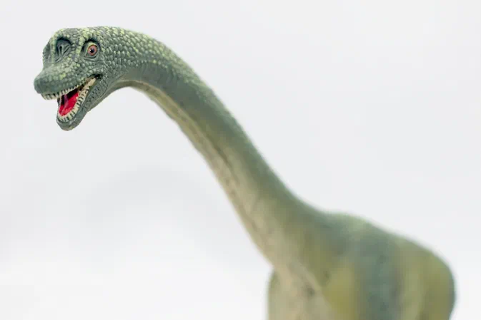 Un dinosaure vert à long cou et tête ouverte sur fond blanc.