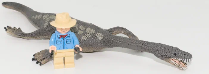 Un dinosaure gris à longues pattes et une figurine Lego d'explorateur en bleu.