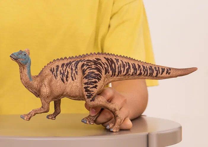Poupée d'Edmontosaure Schleich tenue par une main sur un plateau.