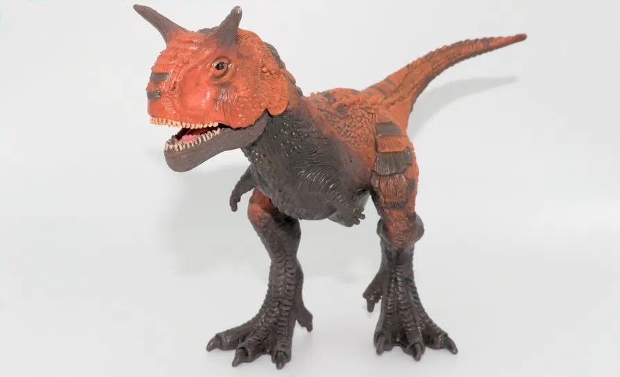 Figurine de dinosaure à deux pattes avec une tête orange et un corps gris sur fond blanc.