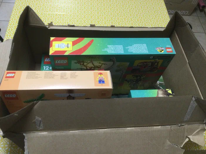 Des boîtes de jeux LEGO sont empilées dans une grande boîte en carton ouverte.
