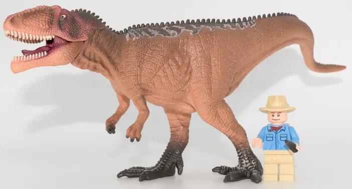 Un jouet de dinosaure T-Rex brun avec un petit personnage Lego à côté.
