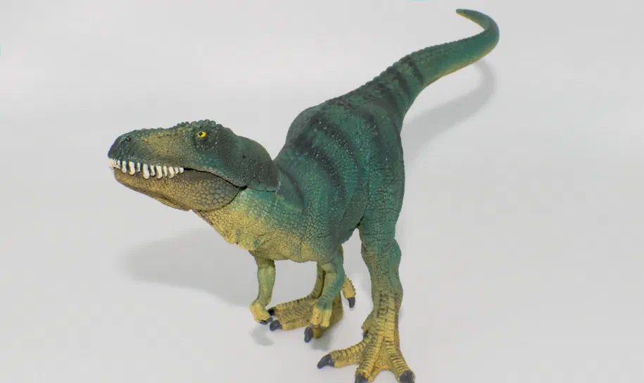 Un jouet de dinosaure vert et jaune à dents blanches sur fond blanc.