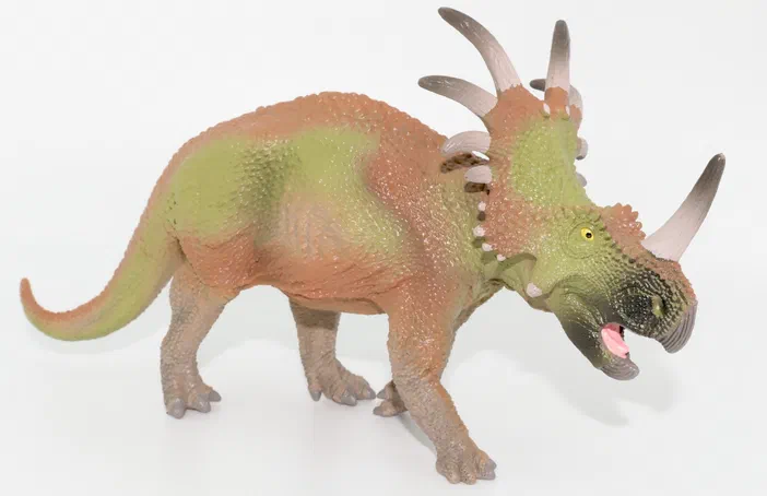 Un jouet de dinosaure triceratops aux couleurs vert et orange sur fond blanc.